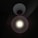 A single bright circular light source is centered within a dark background. The light appears to be an LED bulb encased in a white lampshade that directs the light downwards, creating a halo effect around the light.