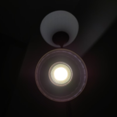 A single bright circular light source is centered within a dark background. The light appears to be an LED bulb encased in a white lampshade that directs the light downwards, creating a halo effect around the light.