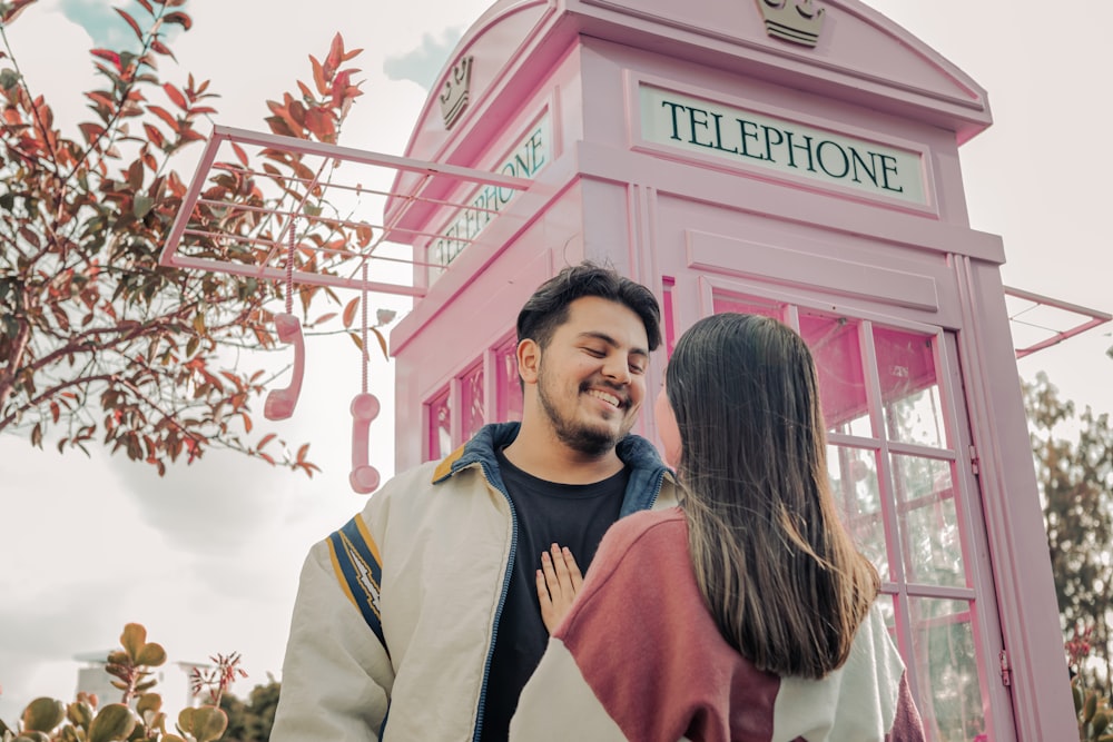 a man and woman standing in front of a pink phone booth