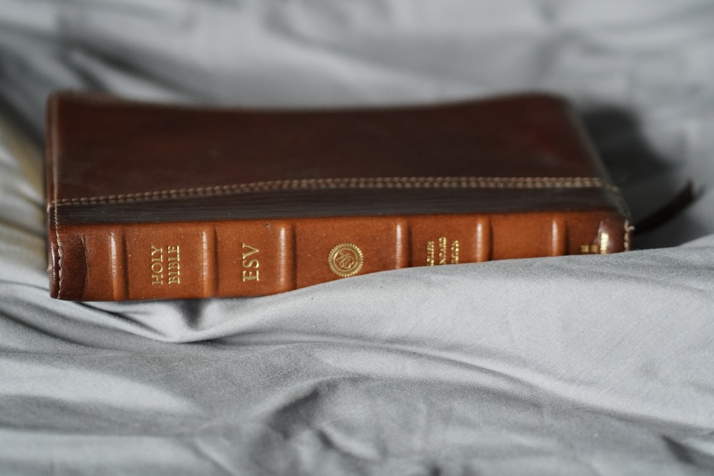 a brown leather book sitting on top of a bed