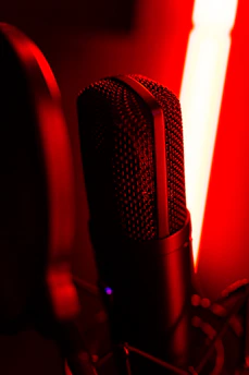 A close-up of a microphone in a dimly lit studio with purple accent lighting.