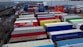 A large industrial storage yard filled with colorful shipping containers and trailers. The containers are stacked and aligned in rows, displaying various brand logos and colors. There are few vehicles parked nearby, and the area seems to be used for logistics or transportation purposes.