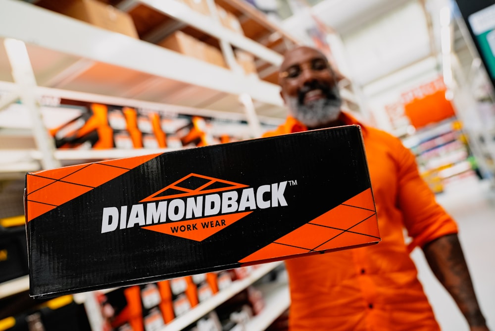 a man in an orange shirt holding a black and orange diamondback sign