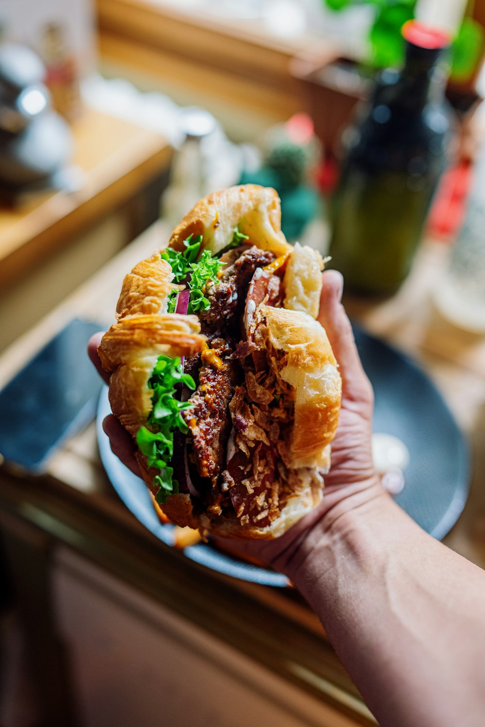 a hand holding a sandwich with meat and lettuce