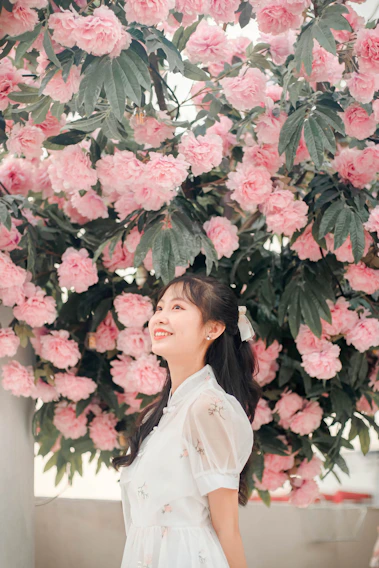 A radiant quinceañera in a flowing pastel pink gown, standing in a sunlit garden.