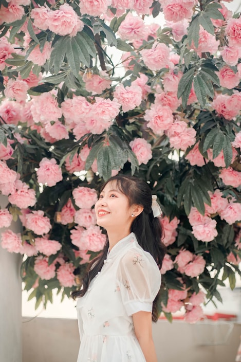 A softly lit photo of a woman wearing a flowing pastel dress, surrounded by delicate flowers.