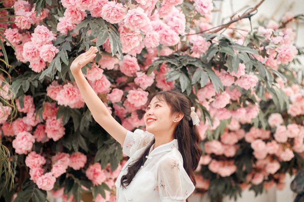 a woman standing in front of a bush of pink flowers