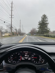 The image captures a view from the interior of a car looking out towards a street. The dashboard is visible, showing a speed of 41 mph. The weather appears overcast with a wet road, suggesting recent rain. There are power lines and trees lining the street.