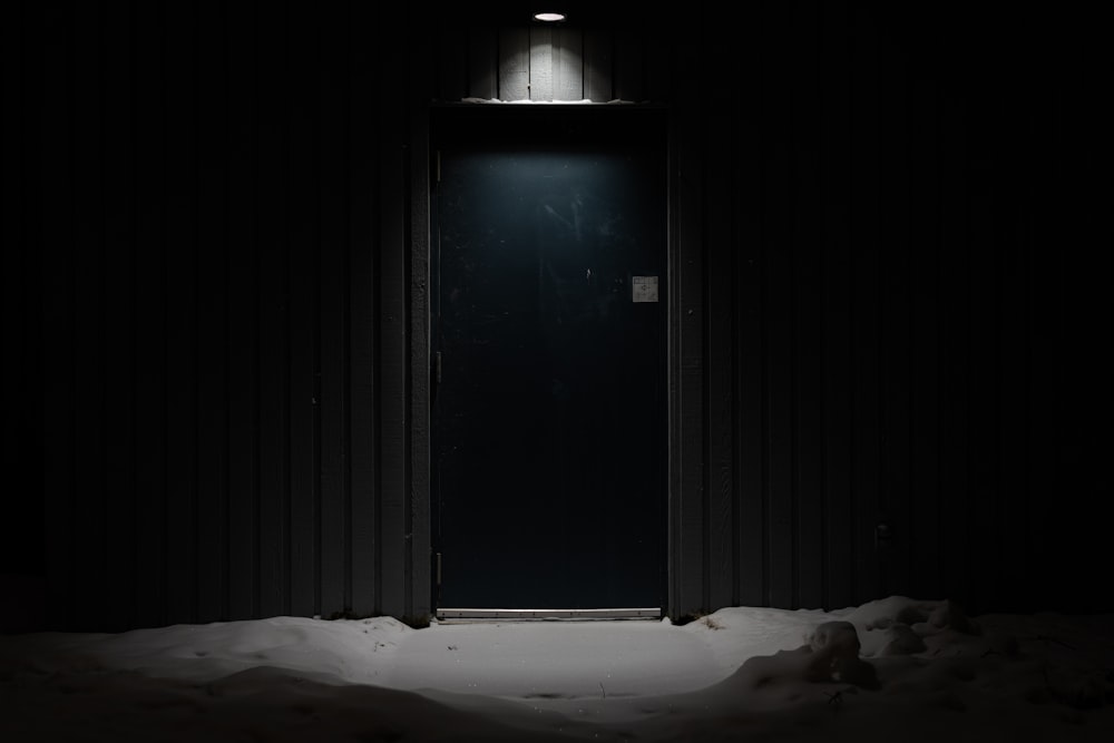 an open door in a dark room with snow on the ground