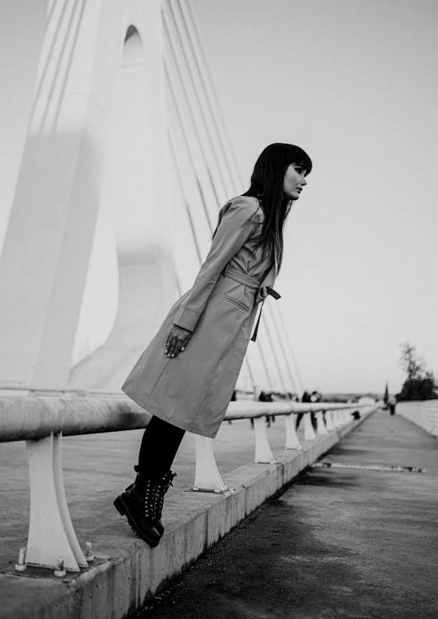 A woman in a trench coat leaning on a railing