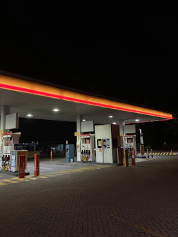 Modern gas station forecourt at dusk with fuel pumps and clear signage.