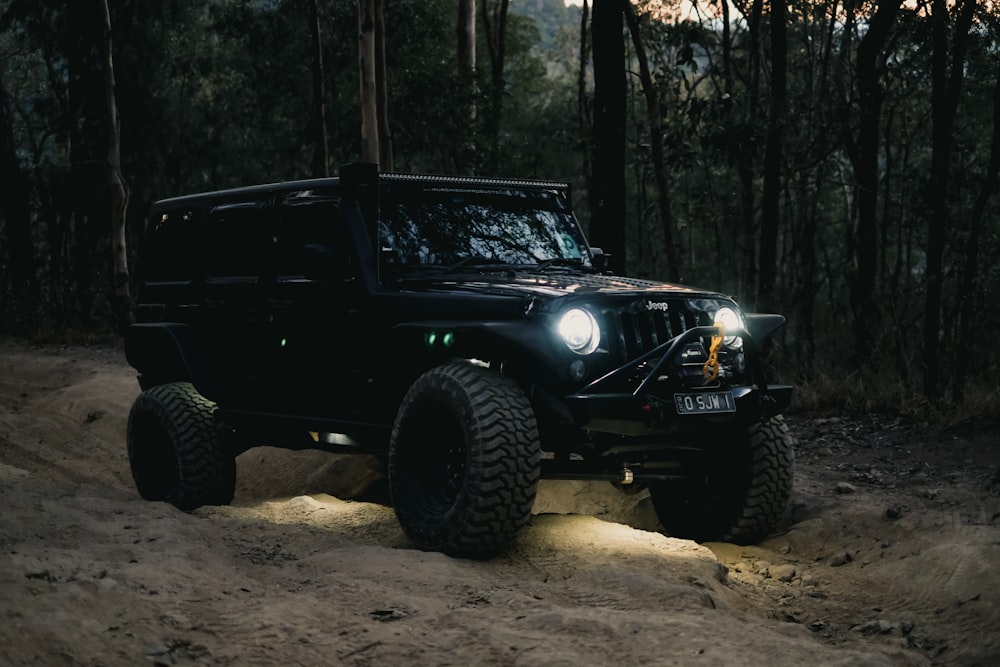 a black jeep driving through a forest at night