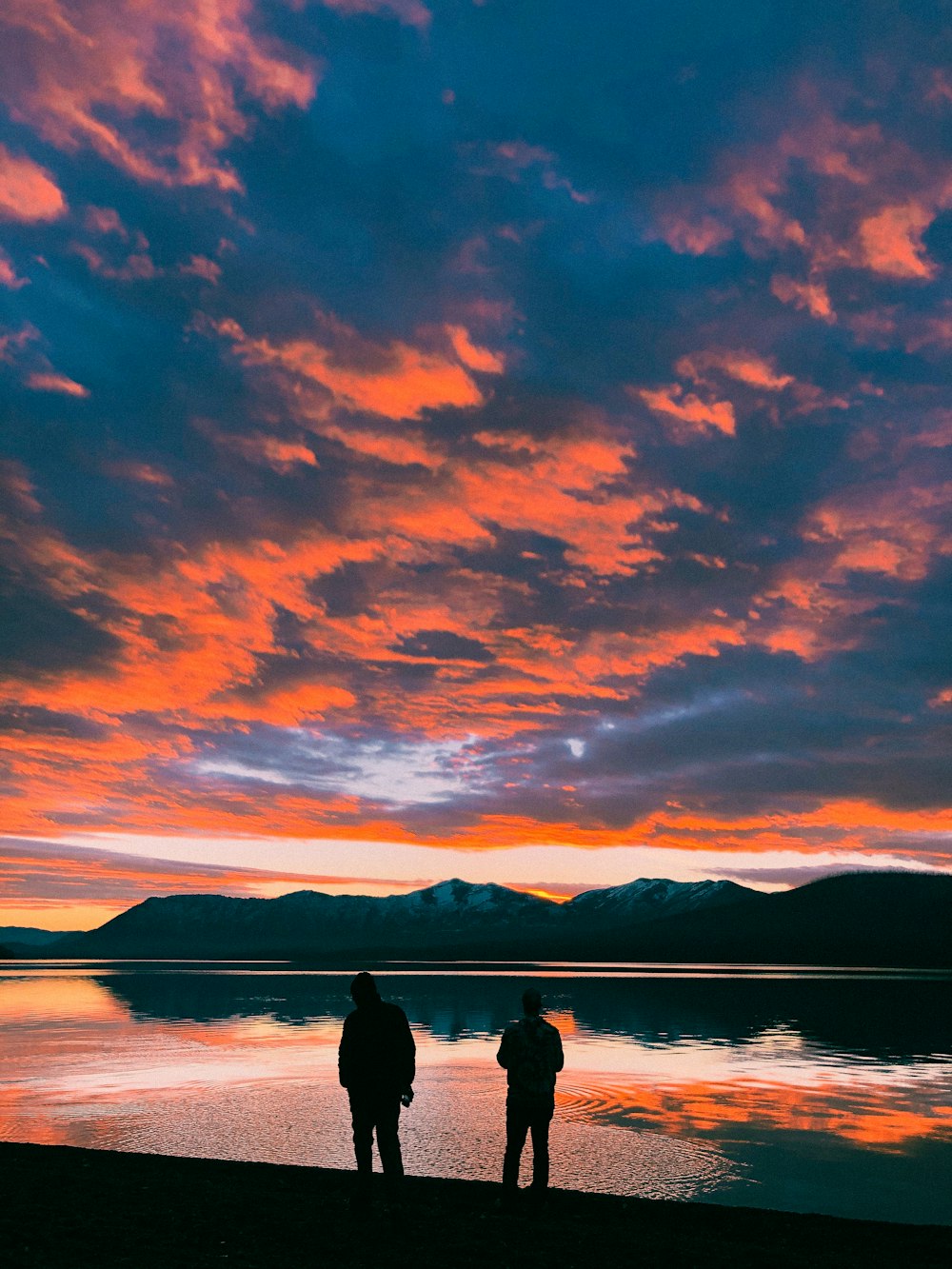 Dos personas de pie en una playa viendo la puesta de sol