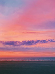 A serene ocean view with a small group of travelers enjoying a sunset on a beach.