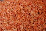 A large pile of dried shrimp with a vibrant orange color, showcasing a texture that appears slightly crispy. The shrimp are small in size and densely packed together, covering the entire image frame.