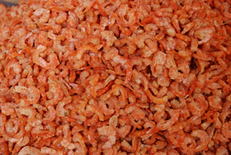 A large pile of dried shrimp with a vibrant orange color, showcasing a texture that appears slightly crispy. The shrimp are small in size and densely packed together, covering the entire image frame.