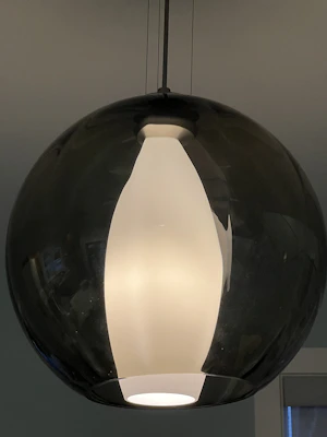 A brutalist-modern style pendant lamp made from stacked glass blocks hanging over a wooden table