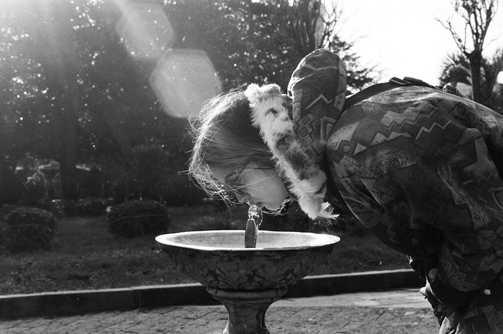 a person bending over to drink from a fountain