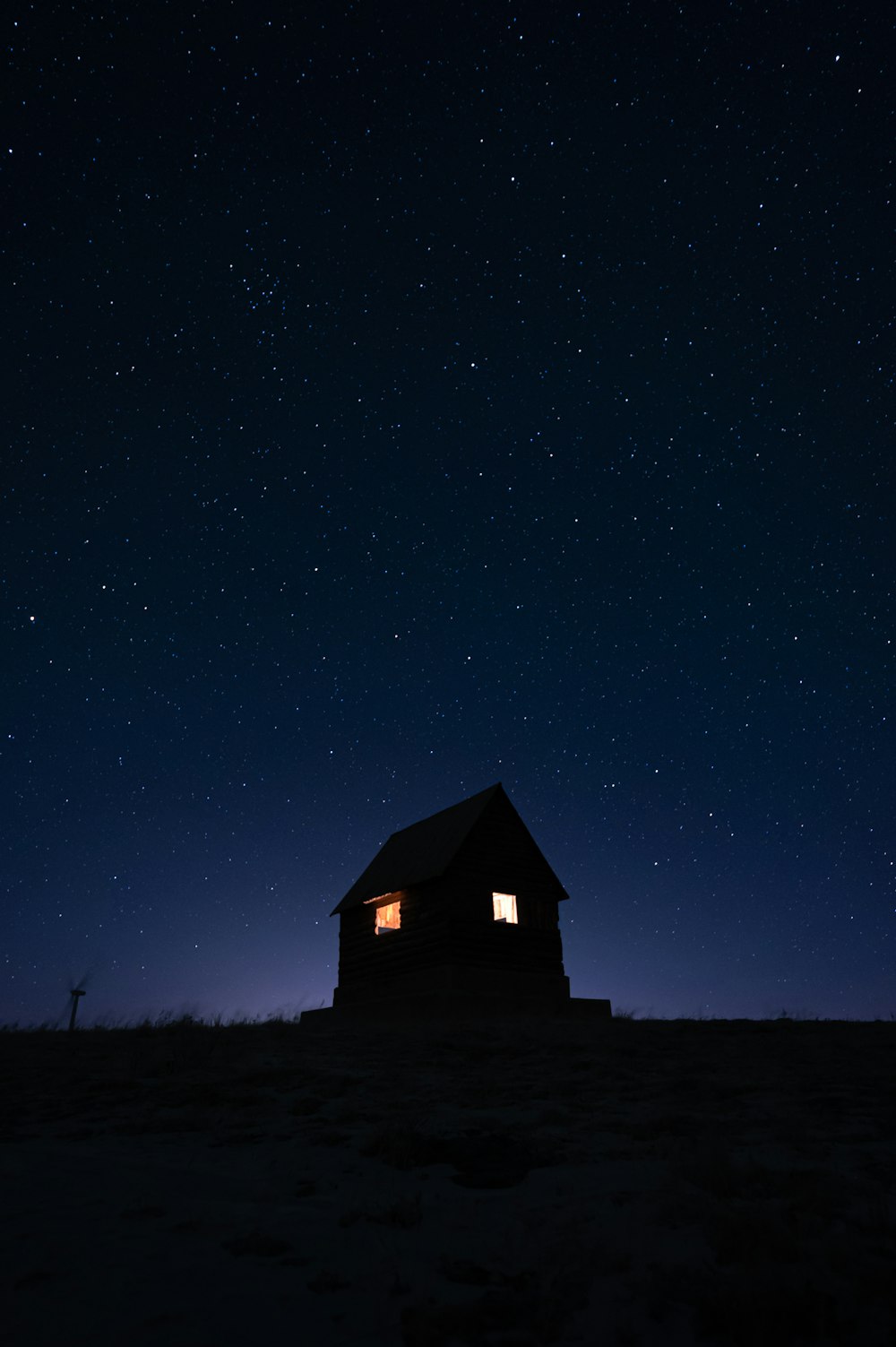 a small cabin sitting in the middle of a field under a night sky