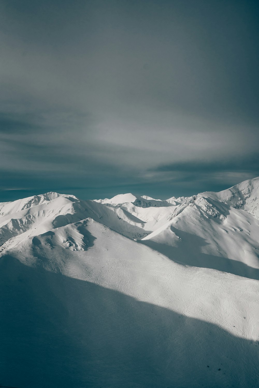 a snow covered mountain range under a cloudy sky