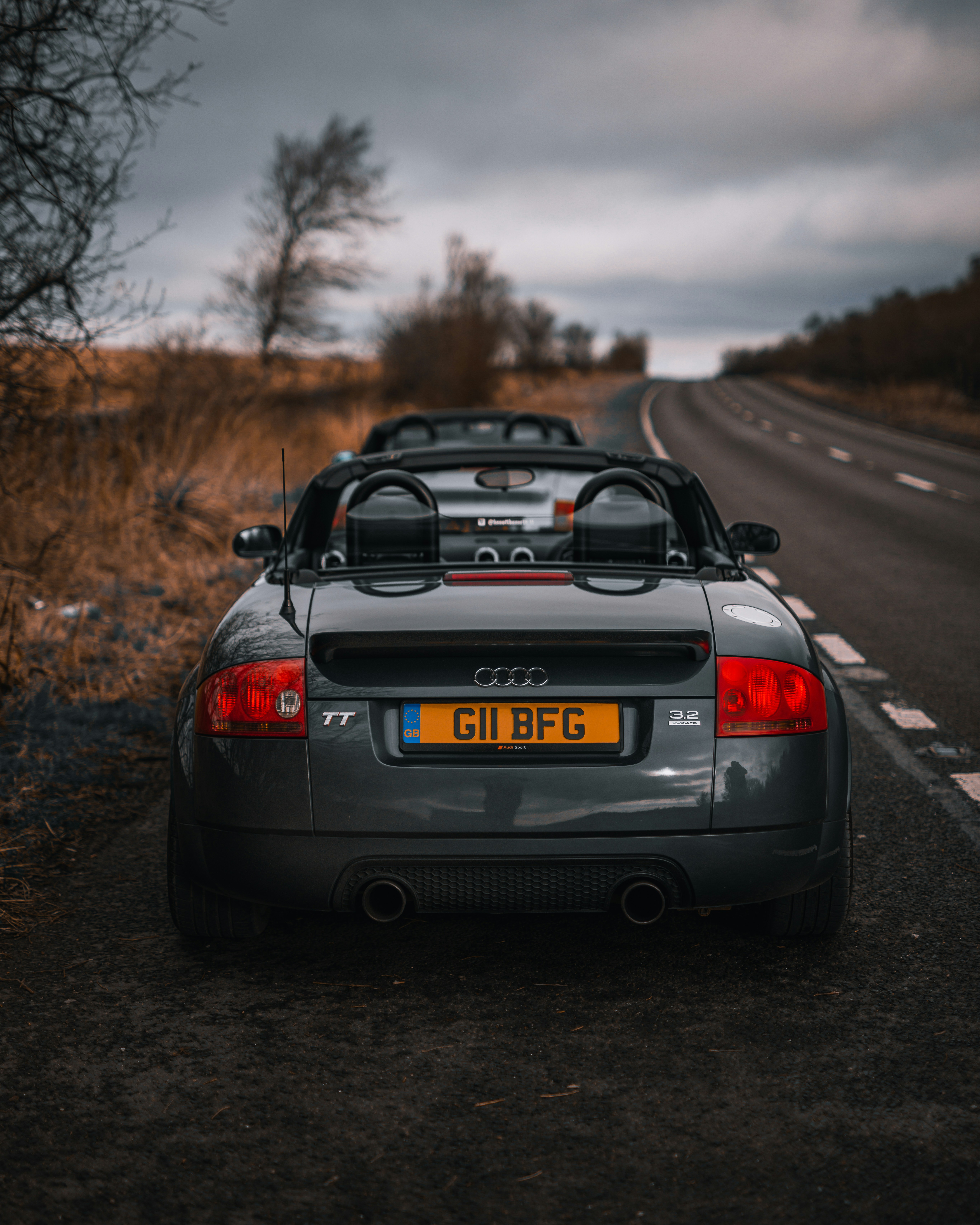 Bentley Continental GT in deep blue with convertible top down, moody overcast sky, dark road, dramatic perspective