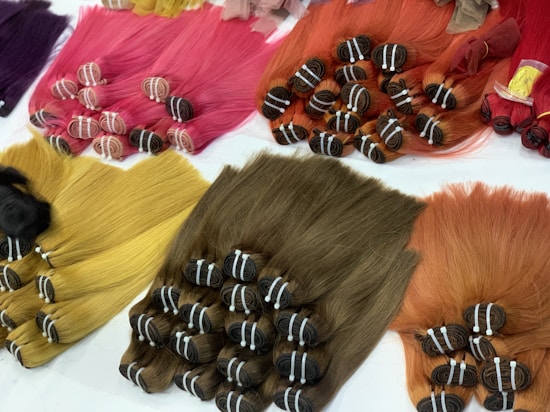 Multiple bundles of hair in a variety of vibrant colors are neatly arranged on a white surface. The colors include pink, red, purple, yellow, and brown. Each bundle is tied securely and appears to be straight and smooth, with the strands lying parallel to one another.