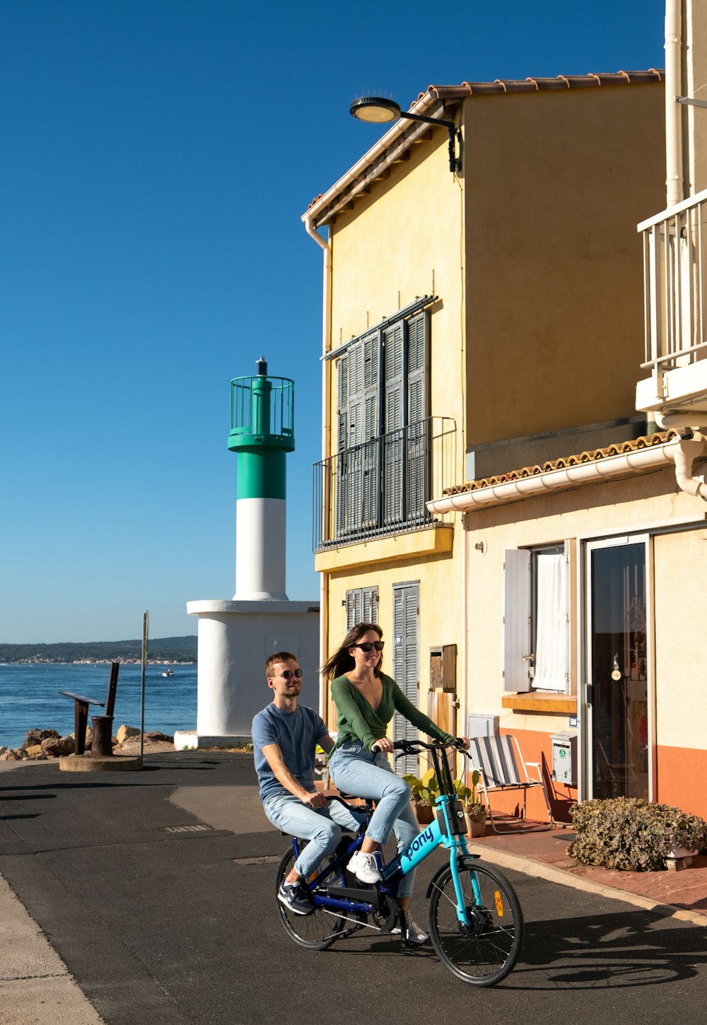 a man and a woman riding a bike next to a light house