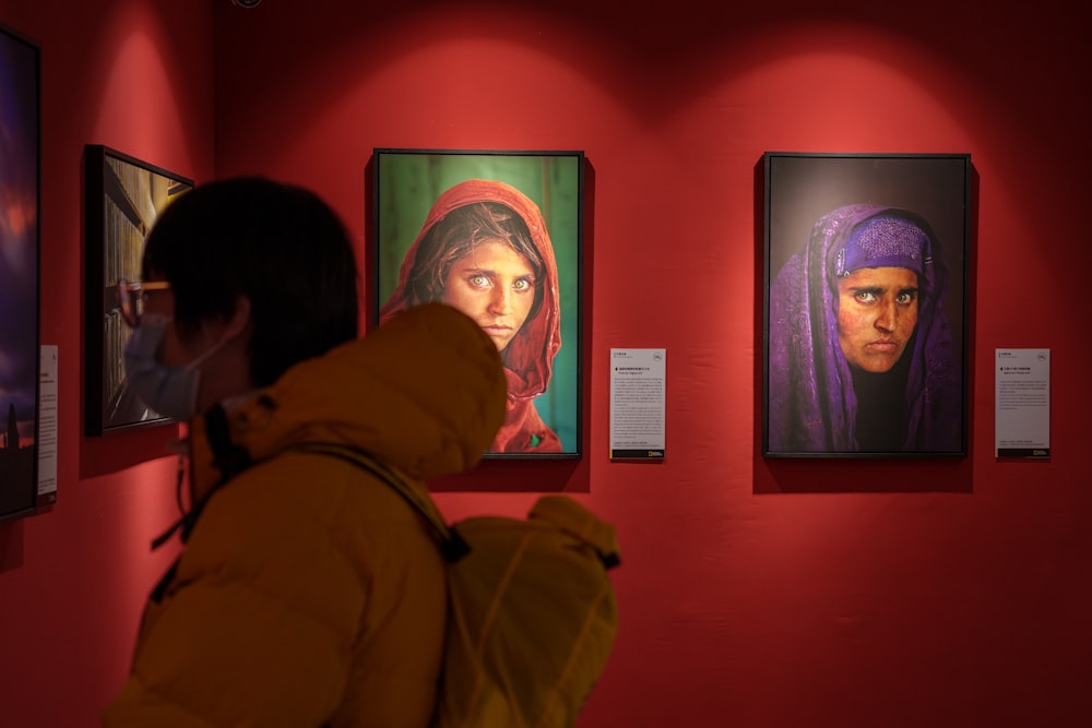 a woman looking at paintings on a red wall