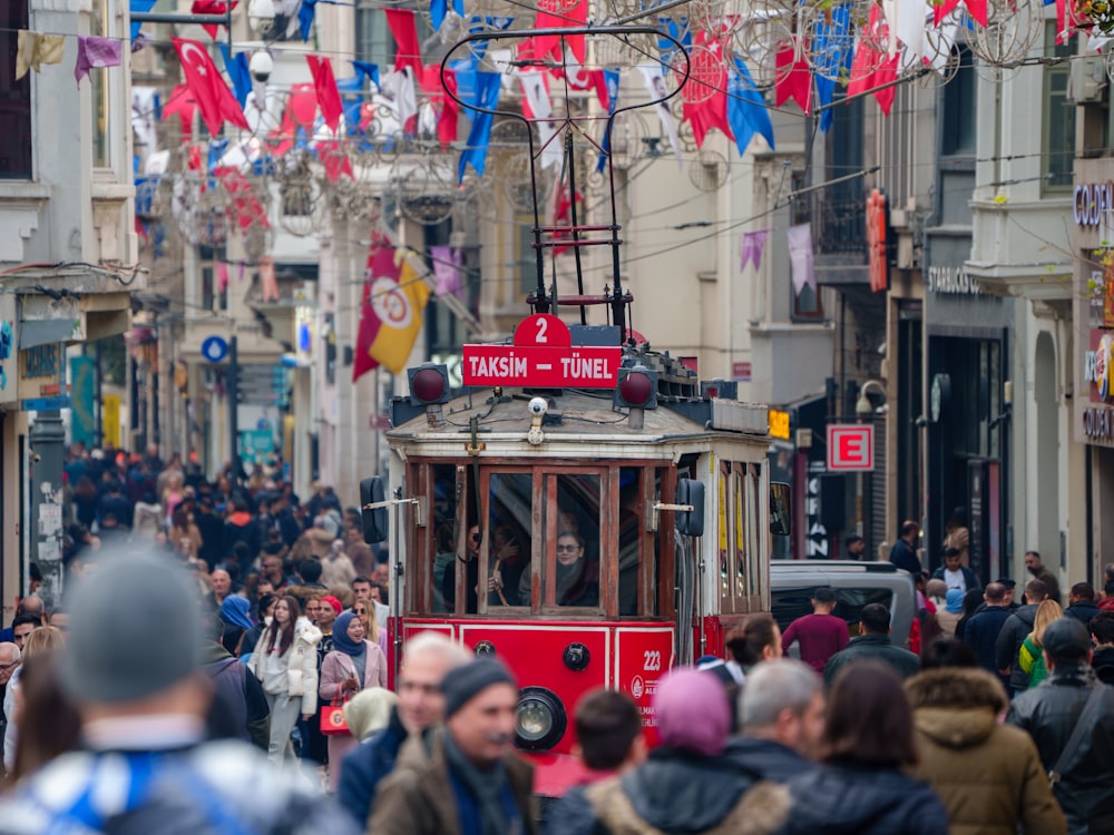 a red trolly car driving down a crowded street