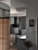 A modern kitchen features sleek cabinetry with light wood and dark finishes, a black range hood, and a gas stove. A counter area includes small kitchen appliances and utensils, with a unique clock on the wall. A decorative wall sign adds a personal touch, and a vase with flowers sits nearby, enhancing the decor.