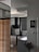 A modern kitchen features sleek cabinetry with light wood and dark finishes, a black range hood, and a gas stove. A counter area includes small kitchen appliances and utensils, with a unique clock on the wall. A decorative wall sign adds a personal touch, and a vase with flowers sits nearby, enhancing the decor.