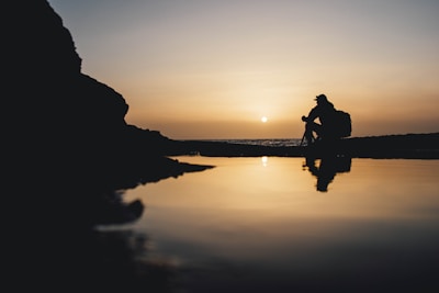 a man sitting on a rock next to a body of water