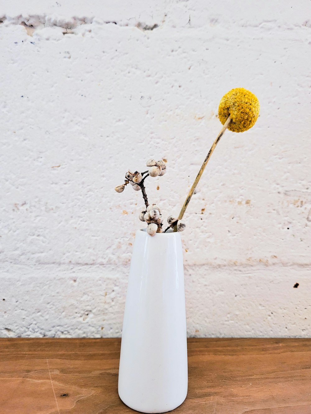 a white vase with a yellow flower in it