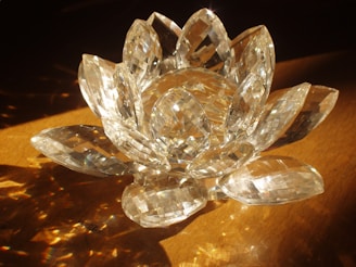 A crystal sculpture resembling a lotus flower, with multiple faceted petals reflecting light on a wooden surface.
