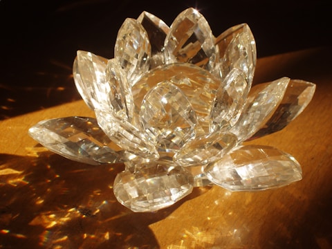 A crystal sculpture resembling a lotus flower, with multiple faceted petals reflecting light on a wooden surface.