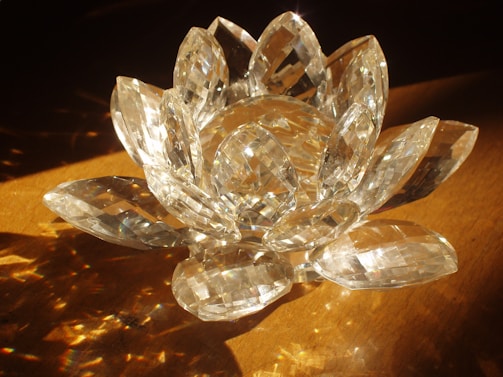 A crystal sculpture resembling a lotus flower, with multiple faceted petals reflecting light on a wooden surface.