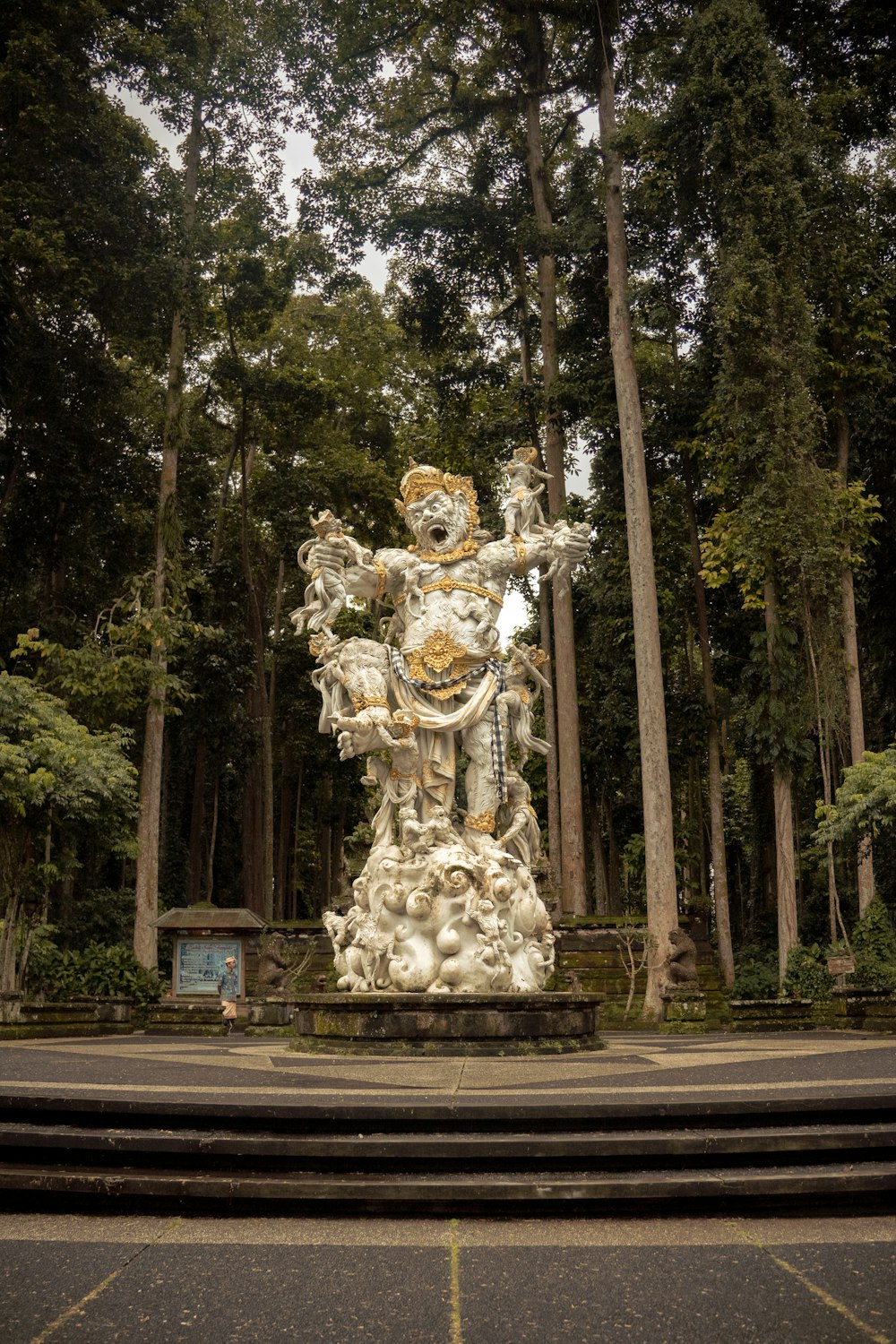 a statue in the middle of a park surrounded by trees