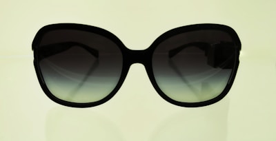 A pair of sunglasses with a reflective lens against a neutral backdrop.