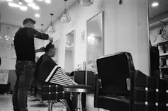 a black and white photo of a barber cutting a customer's hair