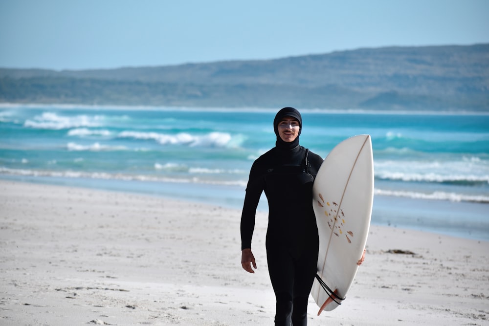 Un homme en combinaison de plongée tenant une planche de surf sur une plage