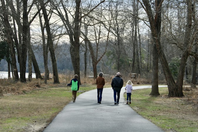 Two people walking together along a paved park path lined with trees and grass