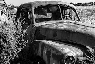 a black and white photo of an old truck in a field