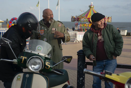 Members gathered around sharing stories and laughter at a lively scooter meetup in a cozy park.