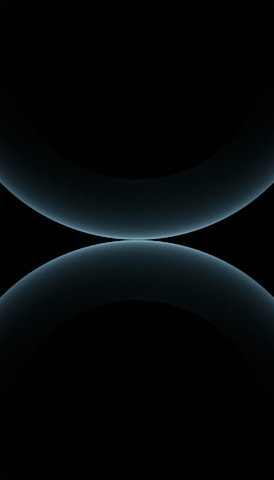 A minimalist design featuring two large, smooth, curved shapes that resemble abstract spheres. The color is a subtle gradient of dark blues against a black background, giving a futuristic and celestial appearance.