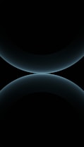 A minimalist design featuring two large, smooth, curved shapes that resemble abstract spheres. The color is a subtle gradient of dark blues against a black background, giving a futuristic and celestial appearance.