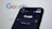 A smartphone displaying the Google search homepage in dark mode, with the Google logo visible on a blurred computer screen in the background.