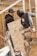 Two construction workers wearing hoodies and tool belts are actively engaged in work at a construction site. One worker is holding a large plywood board, while the other appears to be securing or inspecting structural framing. The background shows unfinished wooden frames, indicating ongoing construction.