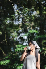 A woman smiling peacefully while sipping tea on a quiet balcony overlooking nature.