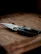Close-up of a bushcraft knife resting on a wooden table with natural foliage background.