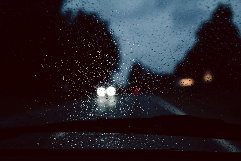 Rain beaded across a windshield at night with oncoming headlights blurred behind it